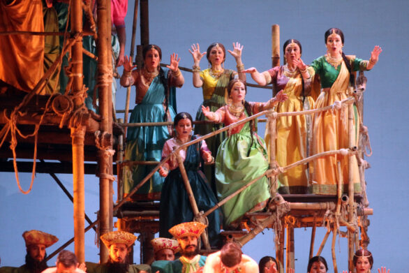 Delle attrici in maschera sono sul palco immerse nei loro personaggi durante l'opera "Les pêcheurs de perles". Si trovano sopra delle impalcature di legno