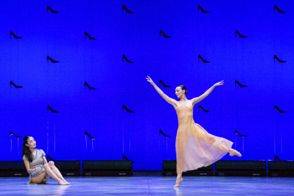 una ballerina sta seduta sul pavimento mentre alla sua destra un'altra ballerina si muove in maniera aggraziata