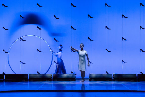 Cenerentola balla al centro del palco, mentre alle sue spalle un'altra figura femminile, illuminata da una luce azzurra, fa ruotare un cerchio