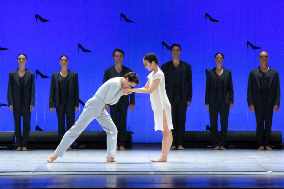 un ballerino vestito di azzurra, bacia la mano di Cenerentola, mentre alle loro spalle si trovano immobili delle figure vestite di nero