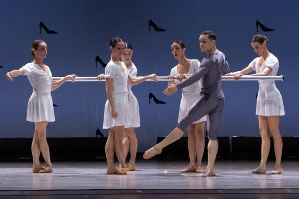 cinque ballerine vestite di bianco ballano con un ballerino vestito di grigio alla sbarra