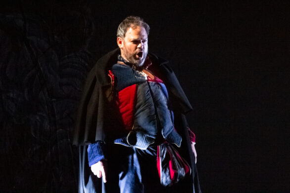 un attore si trova sul palco durante l'opera "Rigoletto". L'uomo è in abito blu e rosso sta cantando