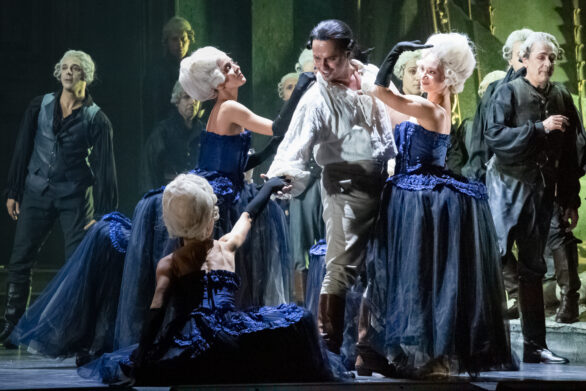 Prospettiva ingrandita del palco. Attori e attrici sono in scena durante l'opera "Rigoletto". Le donne sono vestite in abito blu
