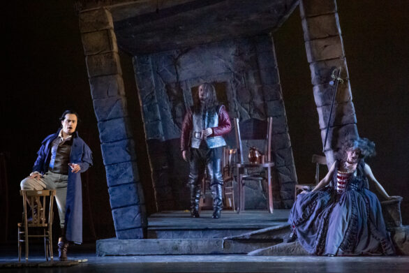 Attori in scena sul palco durante l'opera "Rigoletto". Alle loro spalle si trova una scenografia di una finta parete di mattoni