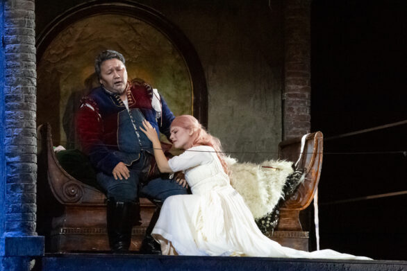 Due attori si trovano sul palco durante l'opera "Rigoletto". Una donna vestita di bianco è poggiata su un uomo seduto su un divanetto