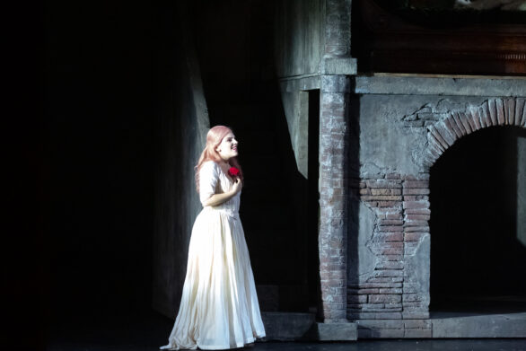 Un'attrice si trova in scena sul palco durante l'opera "Rigoletto". La donna è vestita di bianco e sta tenendo in mano una rosa