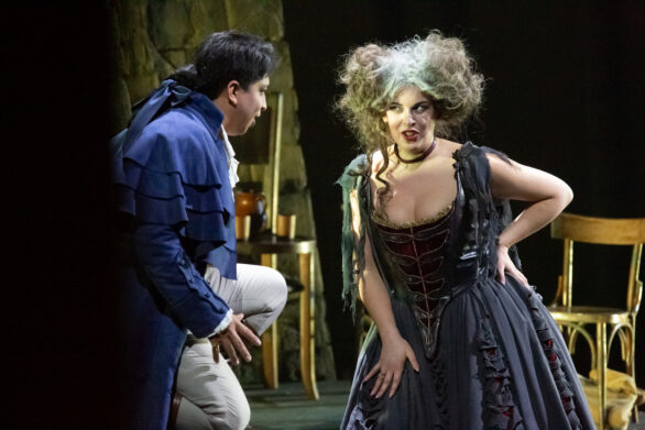 Due attori si trovano sul palco durante l'opera "Rigoletto". La donna indossa una parrucca bianca e un abito blu e sta guardando un uomo