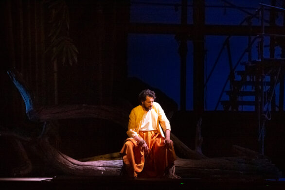 attore sul palco immerso nel suo personaggio durante l'opera "Les pêcheurs de perles". L'uomo si trova seduto su un tronco