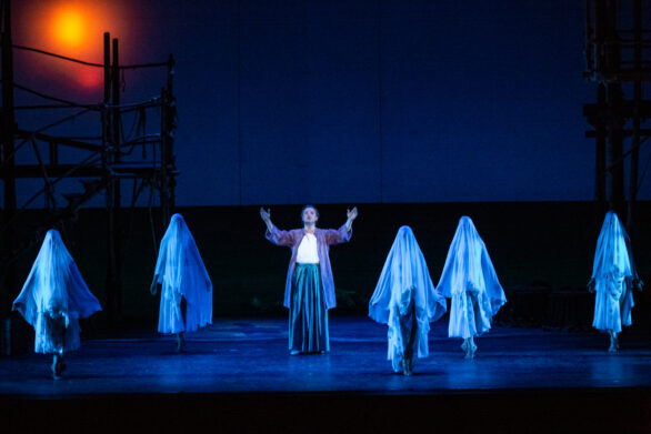 attori sul palco immersi nei loro personaggi durante l'opera "Les pêcheurs de perles". Un uomo si trova al centro del palco, circondato da altri personaggi coperti da un lenzuolo