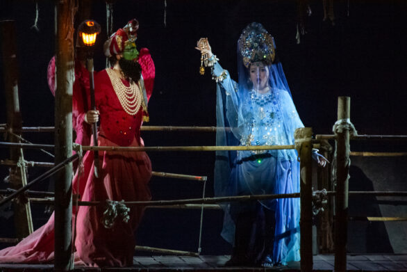 Due attori in maschera sono sul palco immersi nei loro personaggi durante l'opera "Les pêcheurs de perles". Una donna indossa un abito blu, mentre un uomo un abito rosso