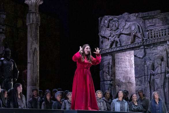 Un donna vestita di rosso sta cantando sopra il palco durante l'opera "Turandot"