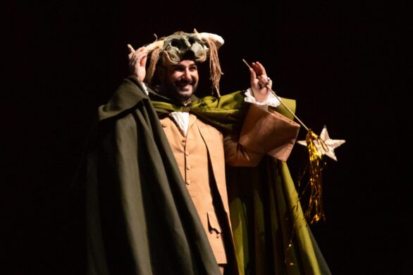 attore in scena ne "Le allegre comari di Falstaff" con un mantello verde, una maschera e una bacchetta magica