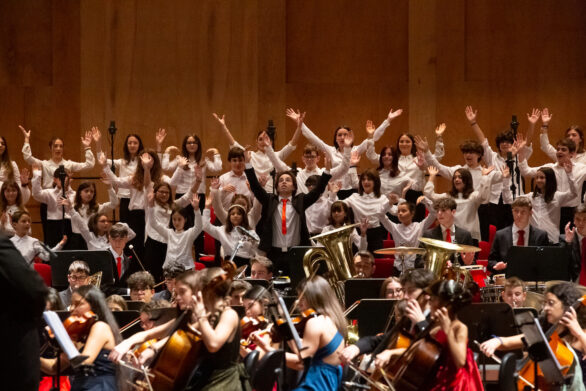 prospettiva frontale dell'orchestra all'interno del teatro durante il concerto di Capodanno delle formazioni giovanili. Il coro di bambini ha le braccia aperte in alto