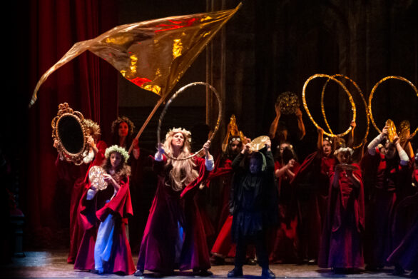 i membri della compagnia teatrale durante una coreografia con oggetti di scena. tra questi oggetti ci sono uno specchio, una bandiera, uno specchio e dei piatti tutti di colore oro.