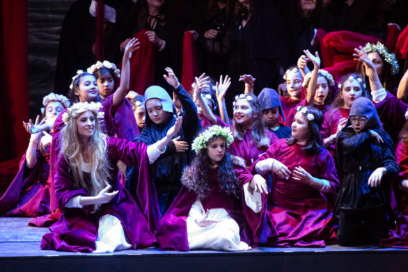 Un gruppo di bambine in veste rossa si trovano sul palco immerse nei loro personaggi