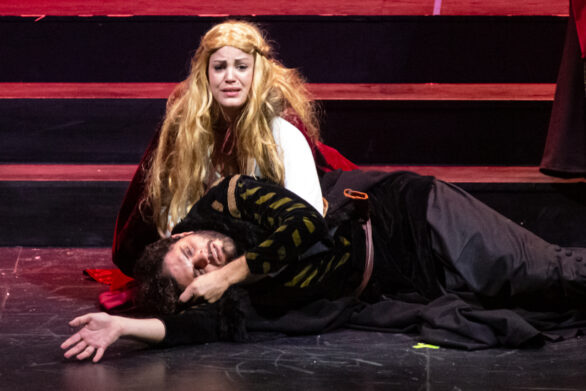 Un uomo e una donna sono in scena sul palco. L'uomo è sdraiato sul palco e sembra avere una faccia dolorante. La donna sembra piangere