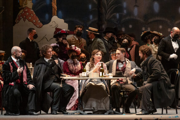 Attori seduti in un tavolo allestito con vino durante l'opera La Boheme