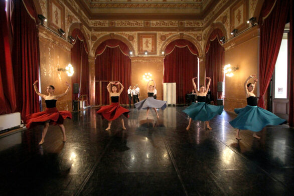 Cinque ballerine all'interno di una sala danzano in abiti lunghi colorati.