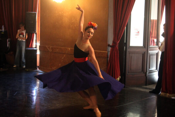 Una ballerina in abito blu con cintura rossa danza in una sala.