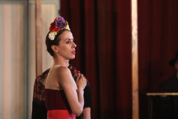 L'attrice interpreta Frida durante lo spettacolo. Indossa un abito con colori scuri tendenti al rosso e una decorazione floreale sulla testa.